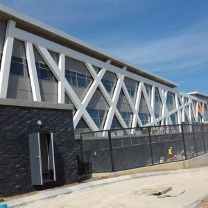 Modern building exterior featuring white architectural framing and perforated building cladding under construction.